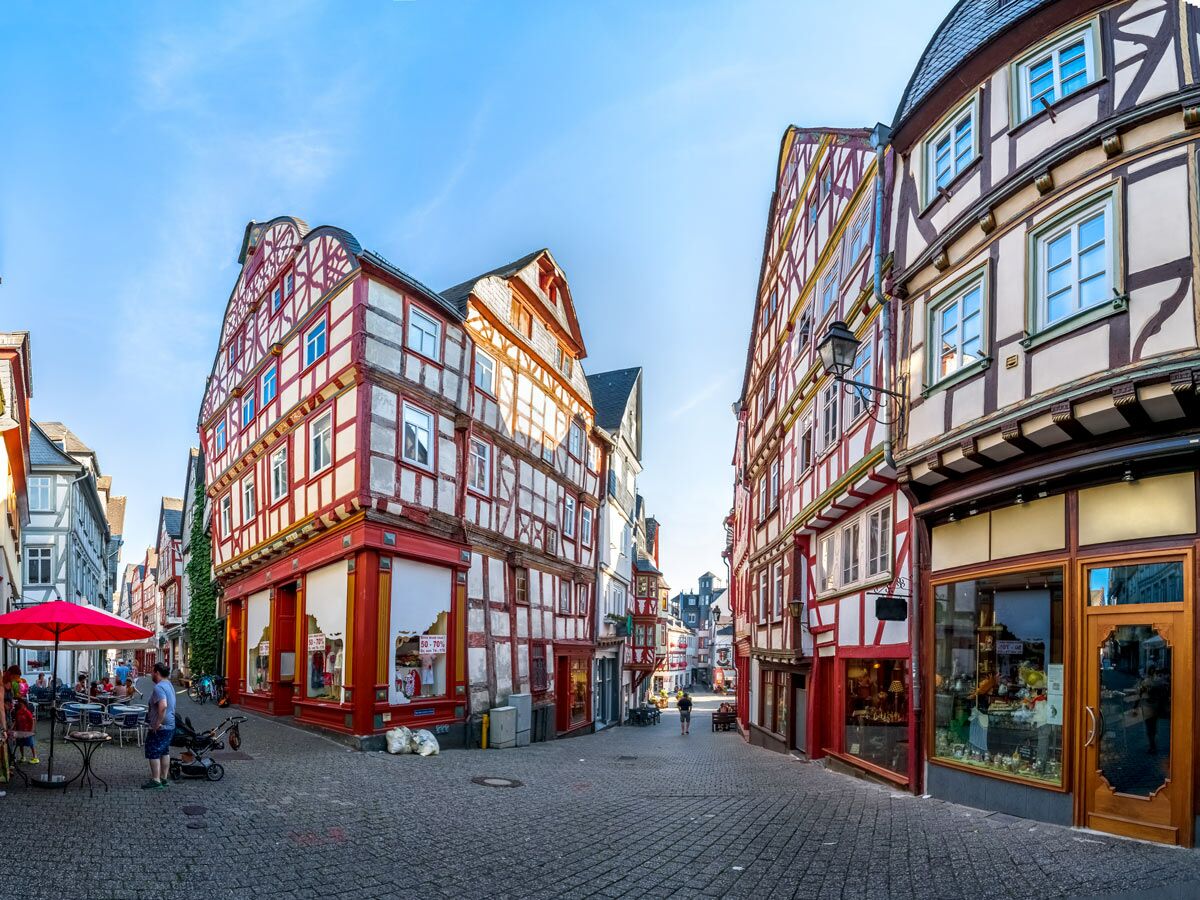 Malerische Gasse mit bunten Fachwerkhäusern, Cafés und Menschen unter blauem Himmel in deutscher Altstadt.