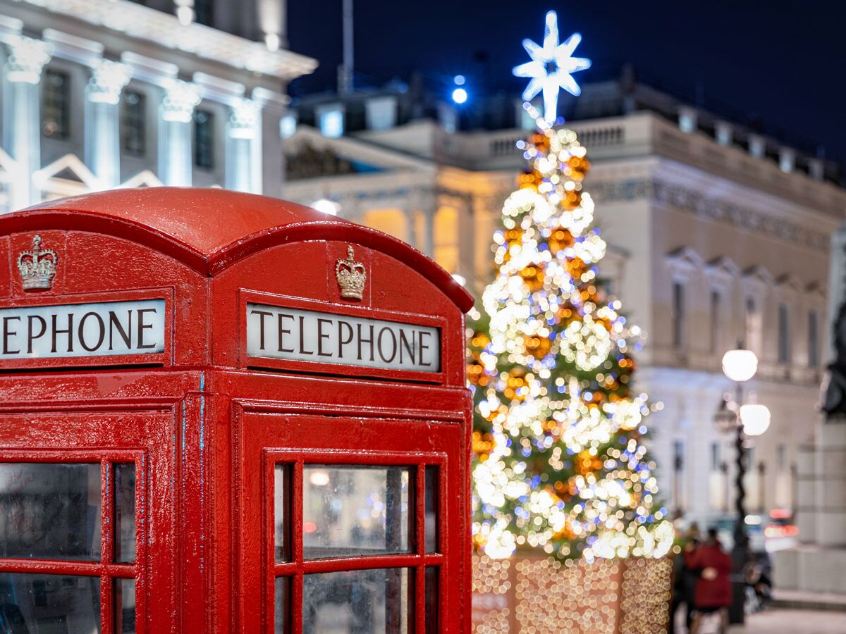 Rote britische Telefonzelle in London vor einem beleuchteten Weihnachtsbaum mit Stern bei Nacht, festliche Stimmung.