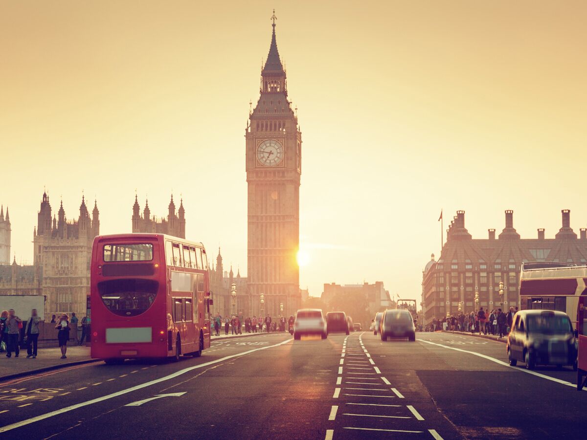 Ikonischer Big Ben und roter Doppeldeckerbus auf der Westminster Bridge bei Sonnenuntergang mit Houses of Parliament.
