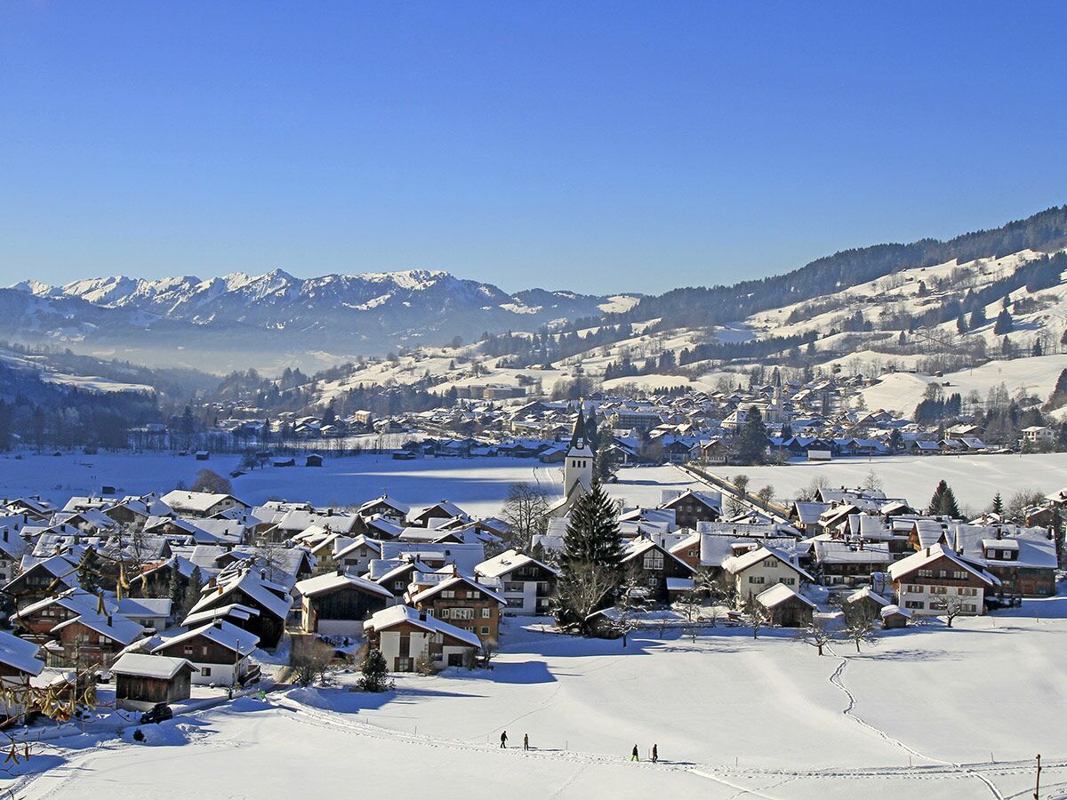 Verschneites Dorf in den Schweizer Alpen bei strahlendem Sonnenschein, mit Bergen im Hintergrund und Spaziergängern im Schnee.
