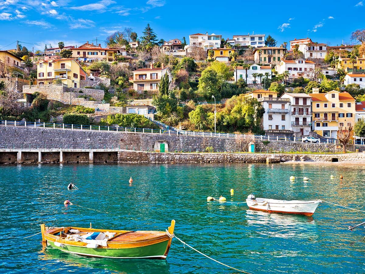 Bunte Häuser einer mediterranen Küstenstadt am Hang über türkisblauem Meer mit traditionellen Fischerbooten.