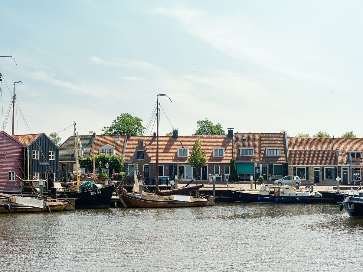 Blick auf einen traditionellen Hafen in den Niederlanden mit vielen Holzbooten, Fischerbooten und bunten Häusern am Ufer unter blauem Himmel.