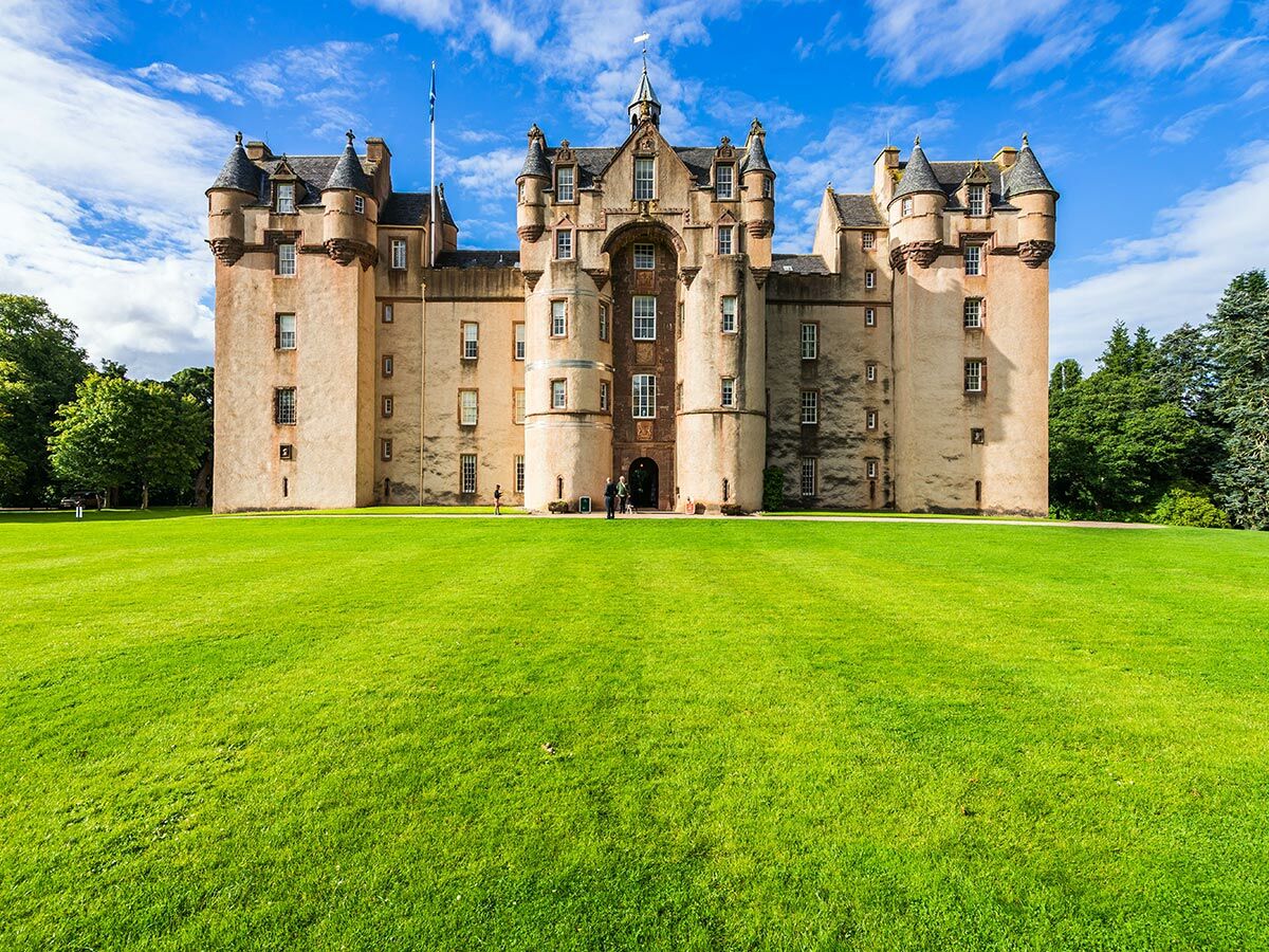 Historisches schottisches Crathes Castle mit rosafarbenen Mauern, Türmen und grünem Rasen unter blauem Himmel.