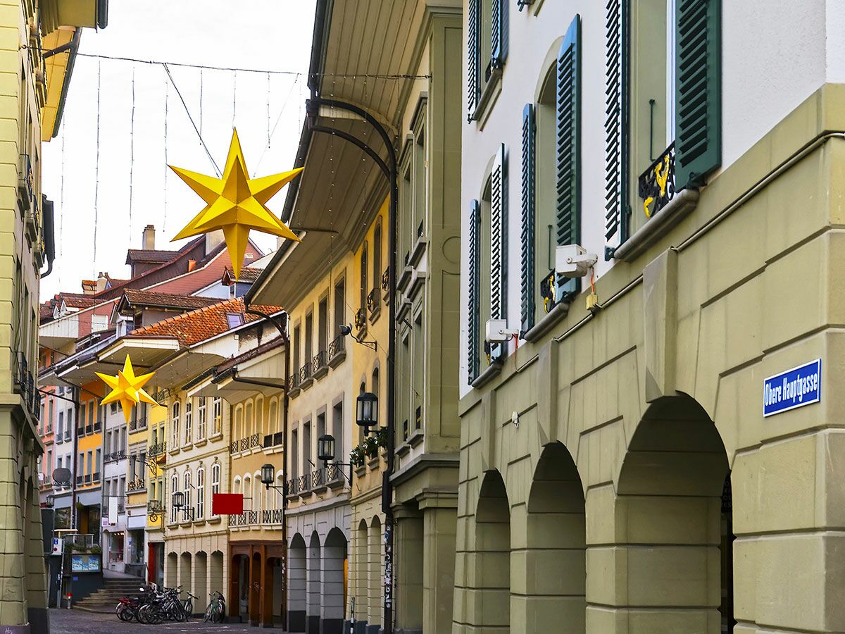 Enge historische Gasse in der Berner Altstadt, geschmückt mit großen gelben Sternen, traditionelle Gebäude mit Arkaden und grünen Fensterläden.