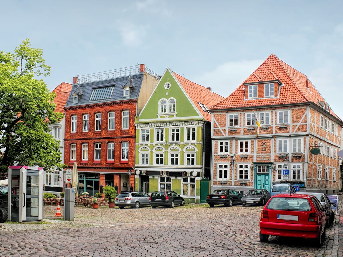 Bunte Giebelhäuser und Fachwerkhäuser an einem historischen Marktplatz mit Kopfsteinpflaster und parkenden Autos in einer europäischen Altstadt.