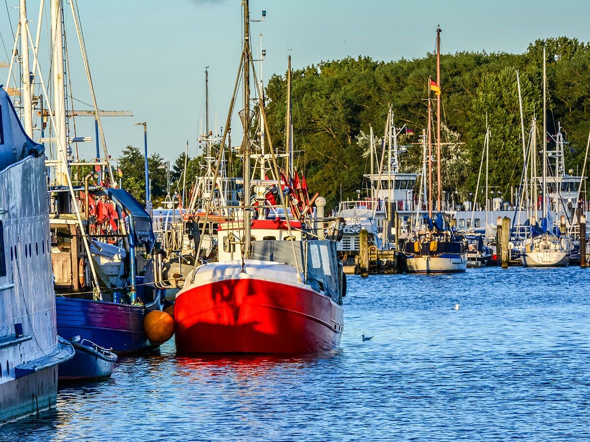 Blick auf einen lebhaften Hafen mit vielen bunten Fischerbooten und Segelyachten bei sonnigem Wetter.