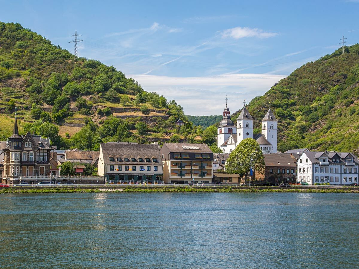 Malerisches Dorf Boppard am Rhein mit prominenter weißer Kirche, bunten Häusern und grünen Terrassenhängen bei Sonnenschein.
