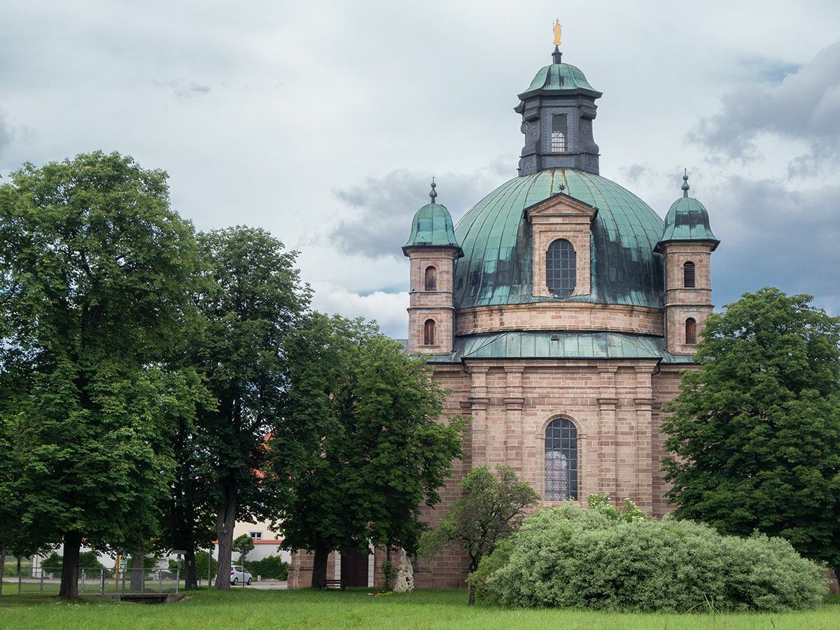 Kloster Banz Basilika, barock, große grüne Kuppel, Sandsteinfassade, Bäume, Wiesen, bewölkter Himmel.