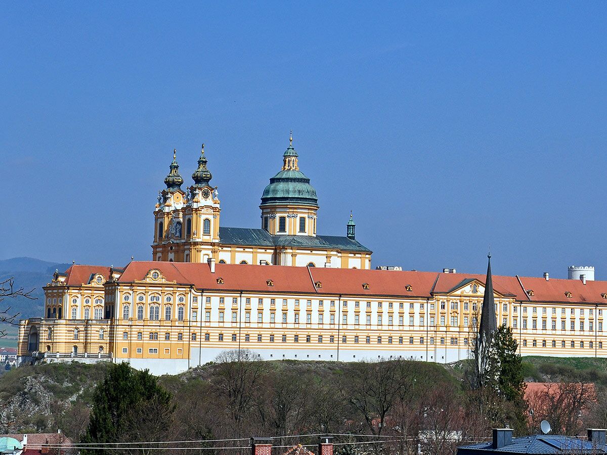 Malerisches Stift Melk in Österreich, ein prächtiges Barockkloster mit goldener Fassade und grüner Kuppel, auf einem Hügel.