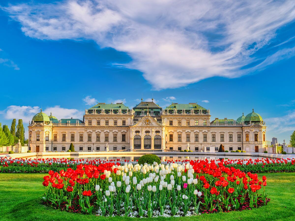 Majestätisches Belvedere Schloss in Wien, umgeben von einem farbenfrohen Frühlingsgarten mit roten und weißen Tulpen.