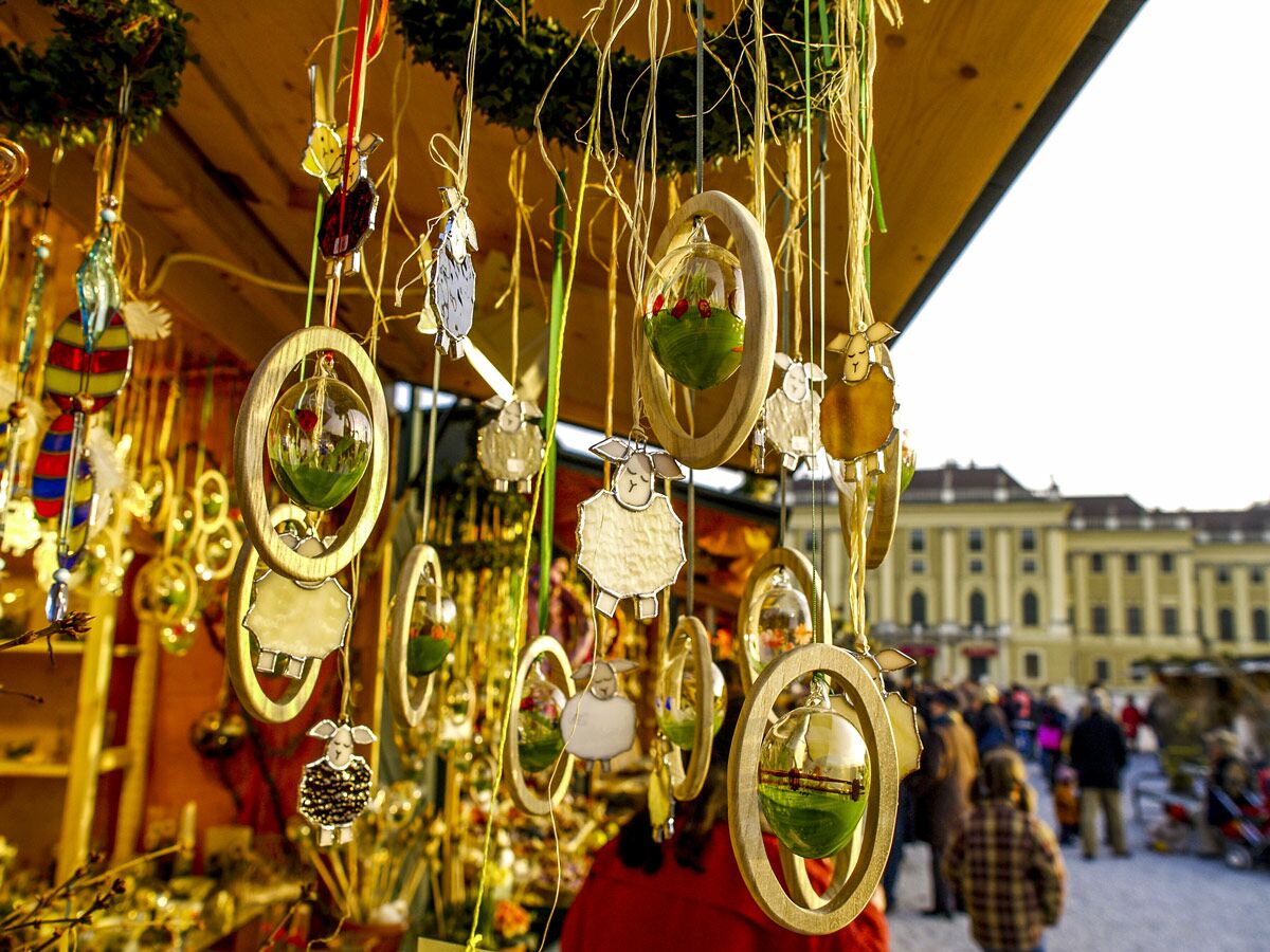 Hängende handgemachte Weihnachtsmarkt-Ornamente, darunter Holzeier mit Glaskugeln und Schafsfiguren, vor Schönbrunn Schloss.