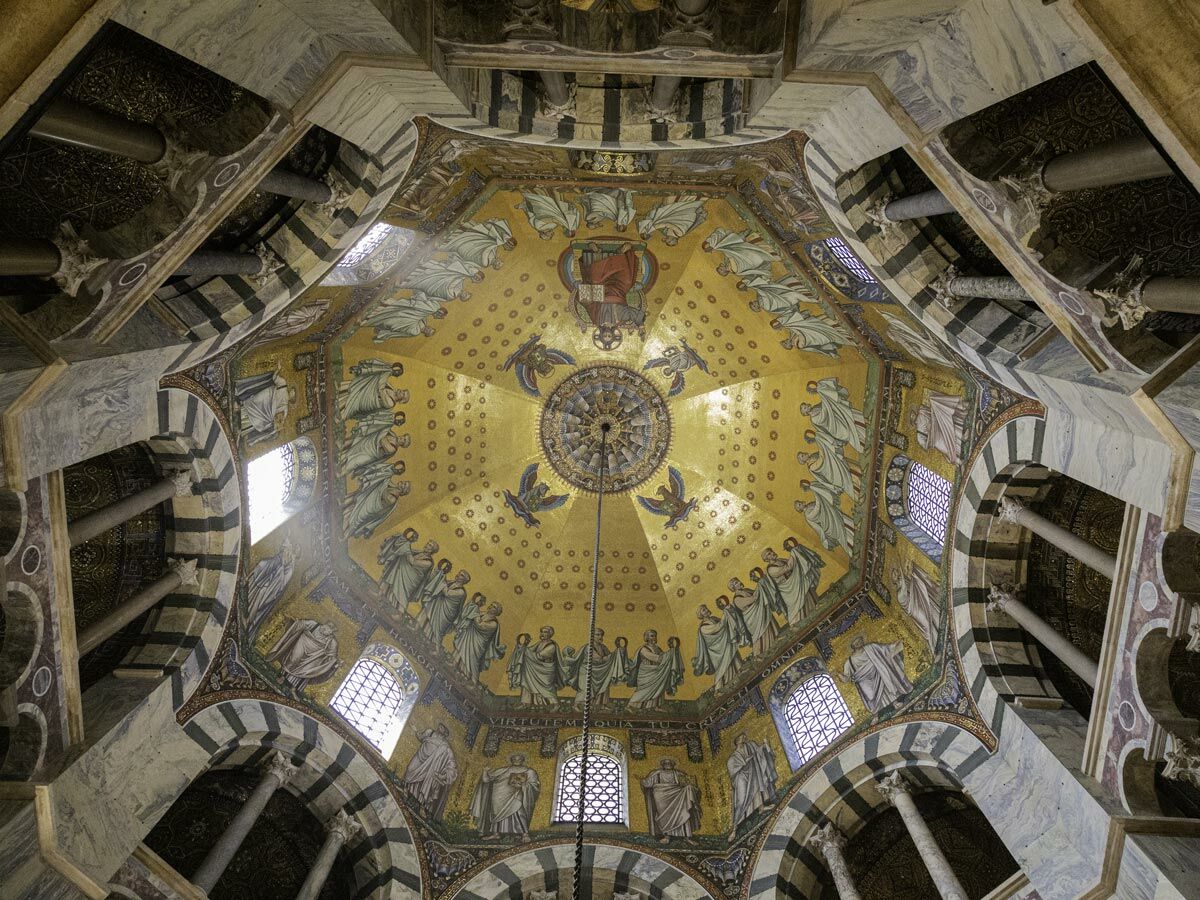 Goldenes byzantinisches Mosaik der Kuppel im Aachener Dom mit Christus Pantokrator, Heiligen und Engeln, umgeben von Marmorsäulen und Bögen.