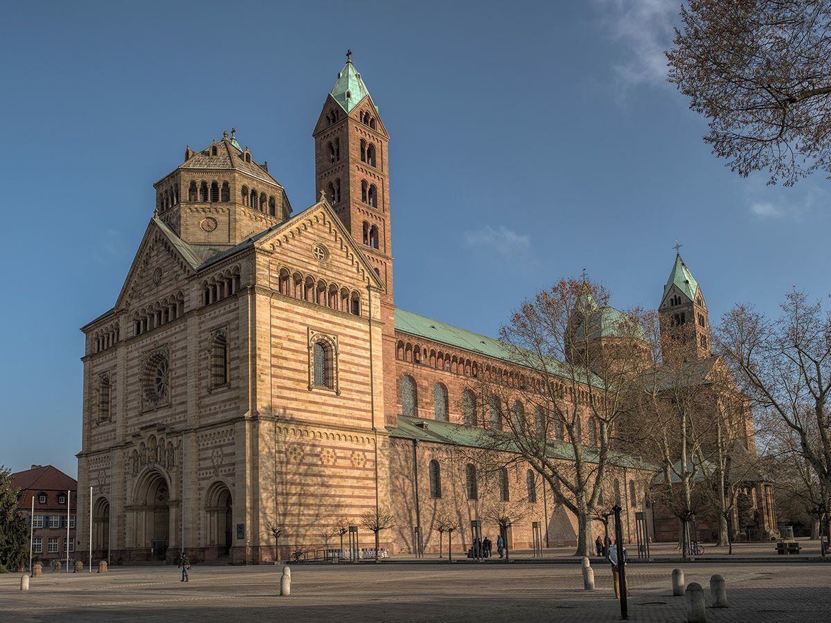 Großer Speyerer Dom, eine romanische Kathedrale aus rötlichem Sandstein mit grünen Dächern unter blauem Himmel, tagsüber.
