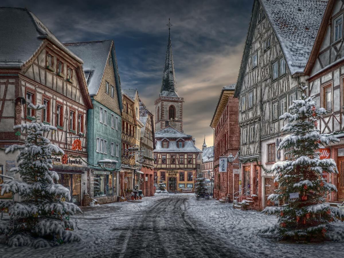 Verschneite Gasse mit Fachwerkhäusern, festlich geschmückten Weihnachtsbäumen und Kirchturm in deutscher Altstadt.