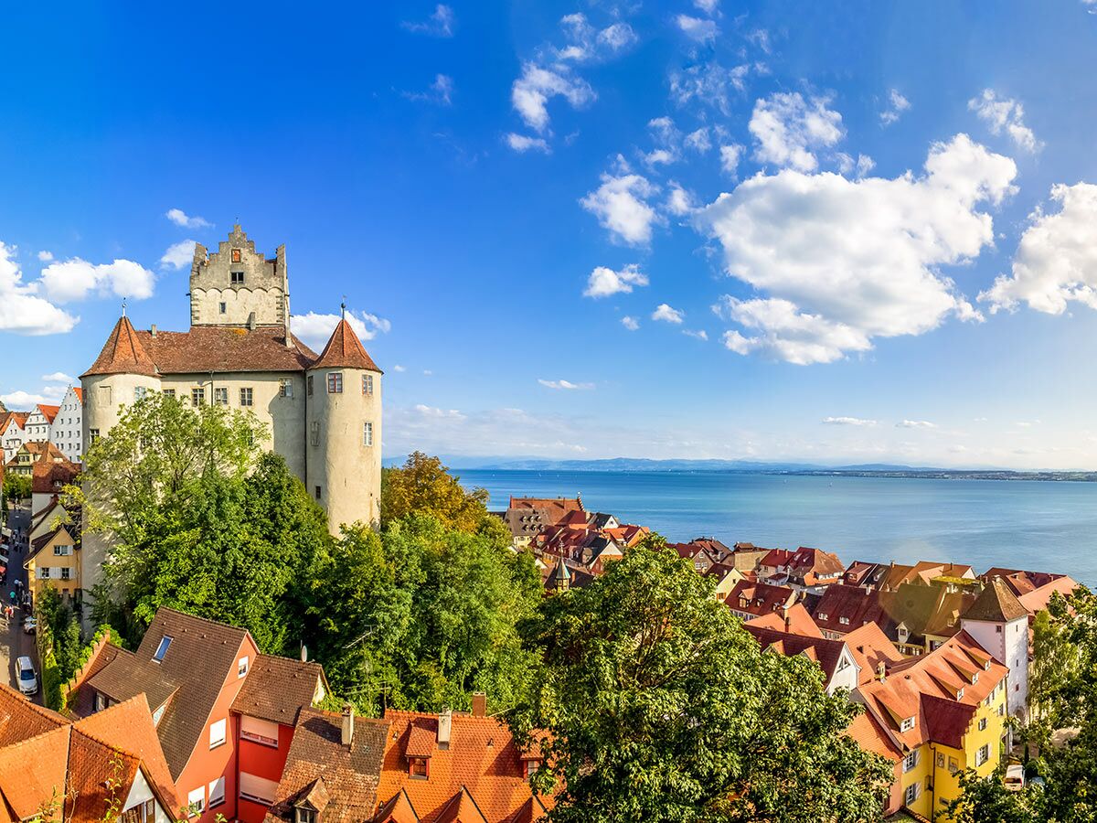 Historisches Schloss Meersburg und Altstadt am Ufer des Bodensees unter blauem Himmel mit Wolken.