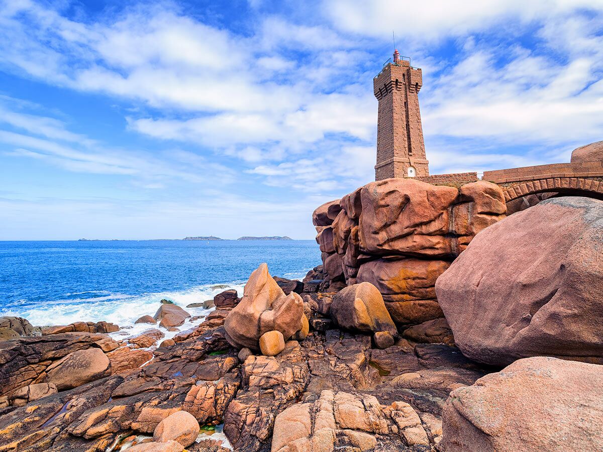 Der Leuchtturm Ploumanac'h auf rosa Granitfelsen an der Küste mit blauem Meer und Himmel in der Bretagne.