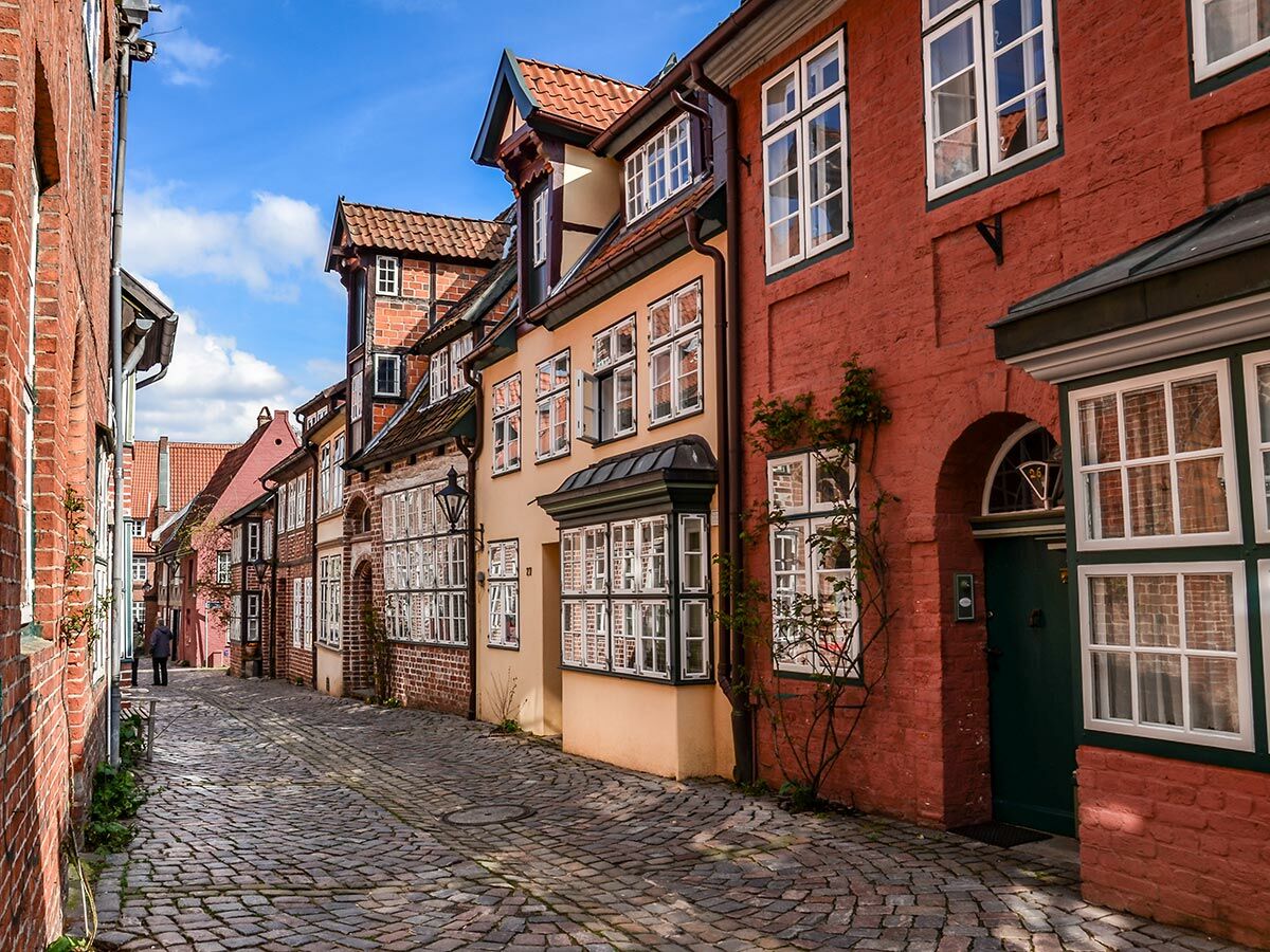 Malerische Kopfsteinpflastergasse mit historischen roten, beigen und Fachwerkhäusern unter blauem Himmel.
