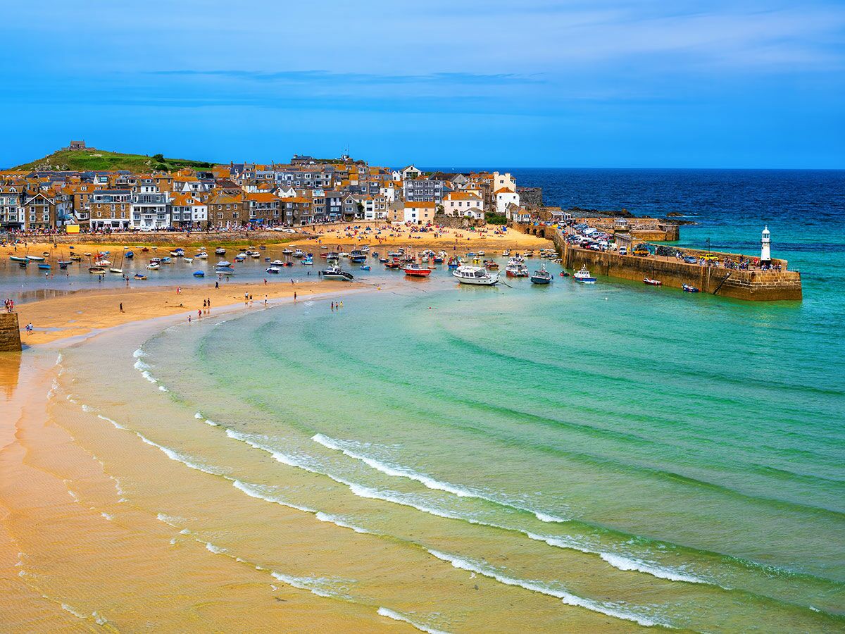 Blick auf St Ives, Cornwall, mit goldenem Sandstrand, türkisblauem Meer, belebtem Hafen voller Boote und malerischer Küstenstadt.