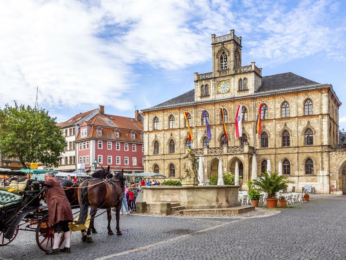 Historischer Marktplatz Gotha mit Rathaus, Pferdekutsche, Brunnen. Menschen flanieren, Cafés laden zum Verweilen ein.