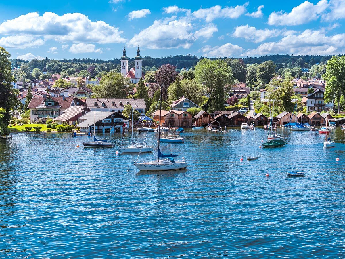 Panoramablick auf ein malerisches Dorf mit bunten Häusern und einer Kirche am Ufer eines blauen Sees mit vielen Segelbooten.