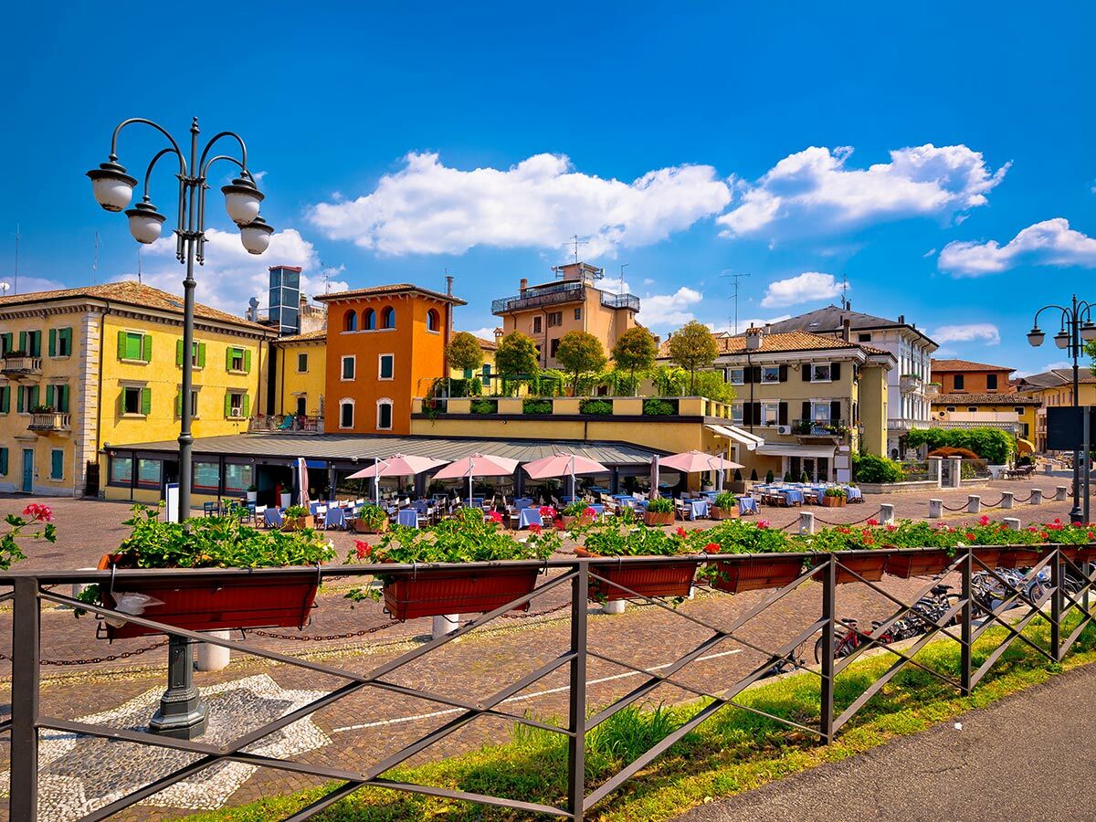 Italienische Altstadt mit farbigen Häusern, belebten Outdoor-Restaurants und blauen Himmel an einem sonnigen Tag.
