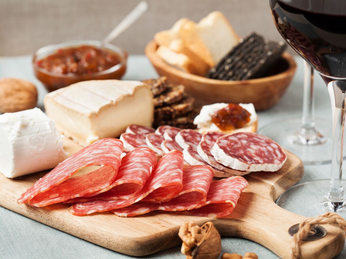 Appetitliches Charcuterie Brett mit Käse, aufgeschnittener Salami, Crackern, Brot, Marmelade und Rotwein im Glas.