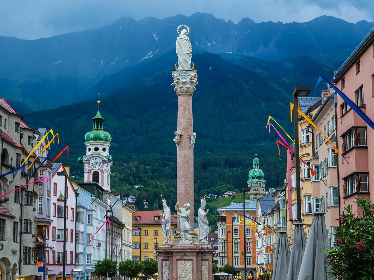 Blick auf die Annasäule in Innsbruck mit Maria-Statue, umgeben von bunten Häusern und Alpenpanorama im Hintergrund.