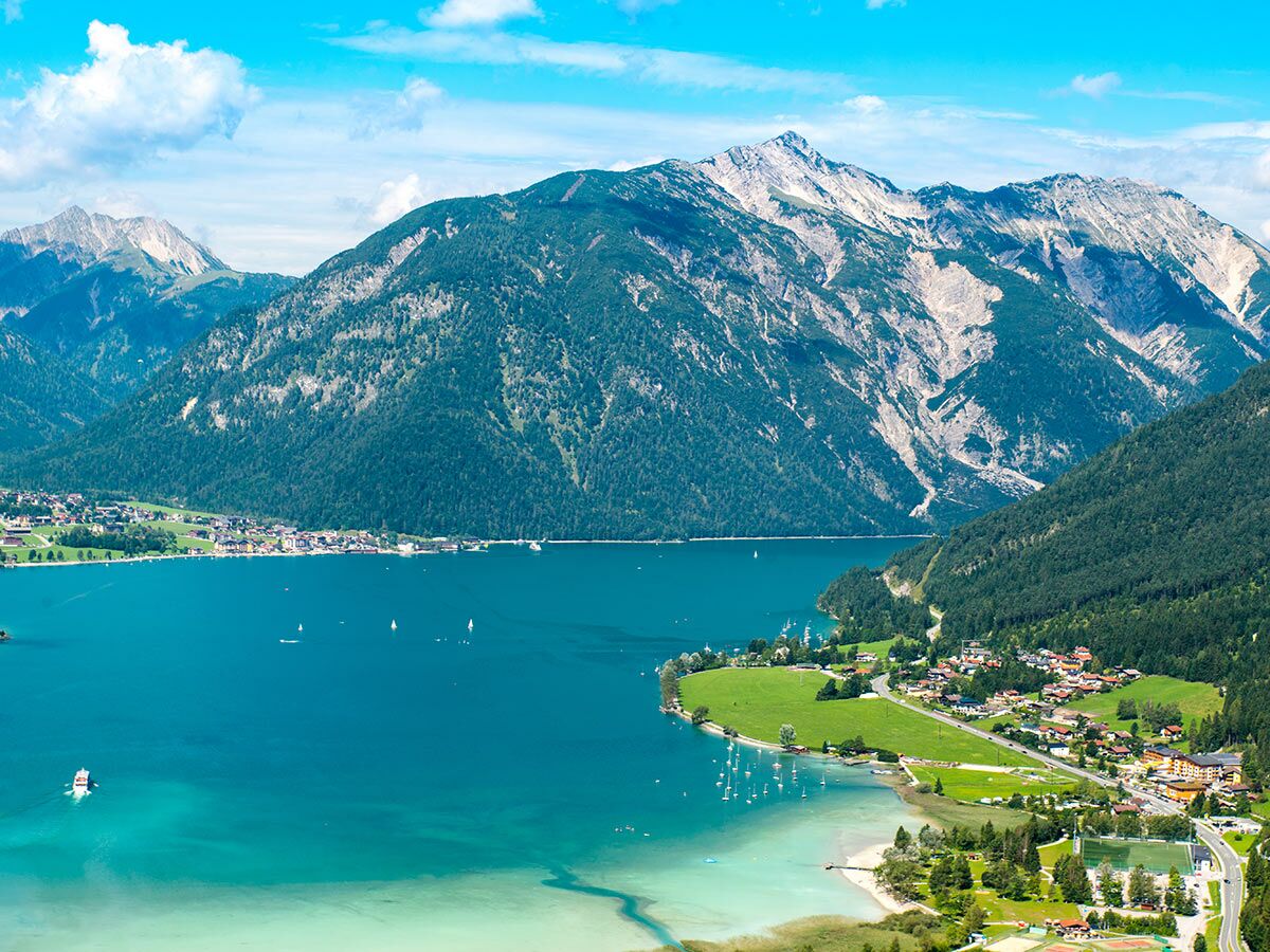 Panorama des türkisen Achensees in Tirol, Österreich, mit Booten, Uferdörfern und bewaldeten Alpenbergen.
