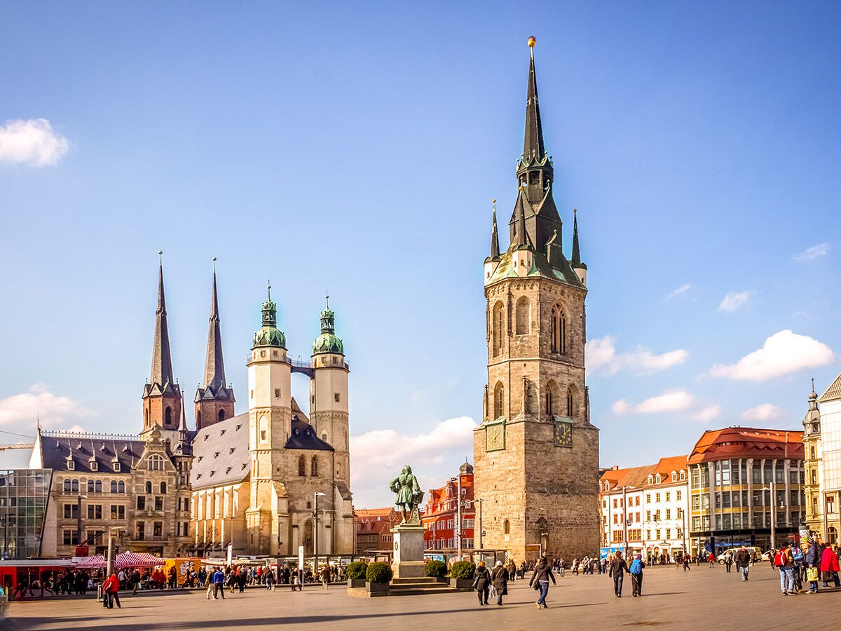 Historischer Marktplatz in Halle an der Saale mit Marktkirche, Rotem Turm, Händel-Denkmal und belebter Atmosphäre unter blauem Himmel.