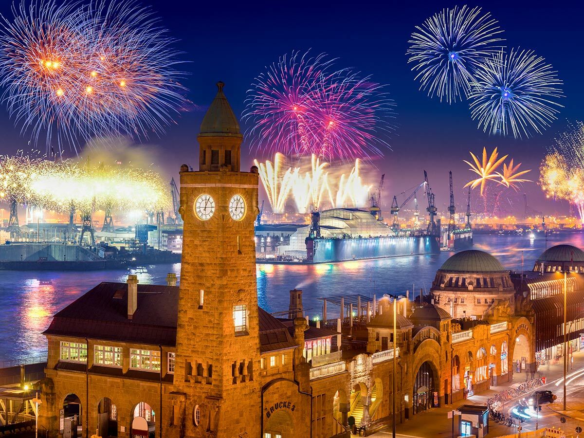 Spektakuläres Feuerwerk über dem Hamburger Hafen bei Nacht, mit beleuchtetem Uhrenturm und St. Pauli Landungsbrücken.