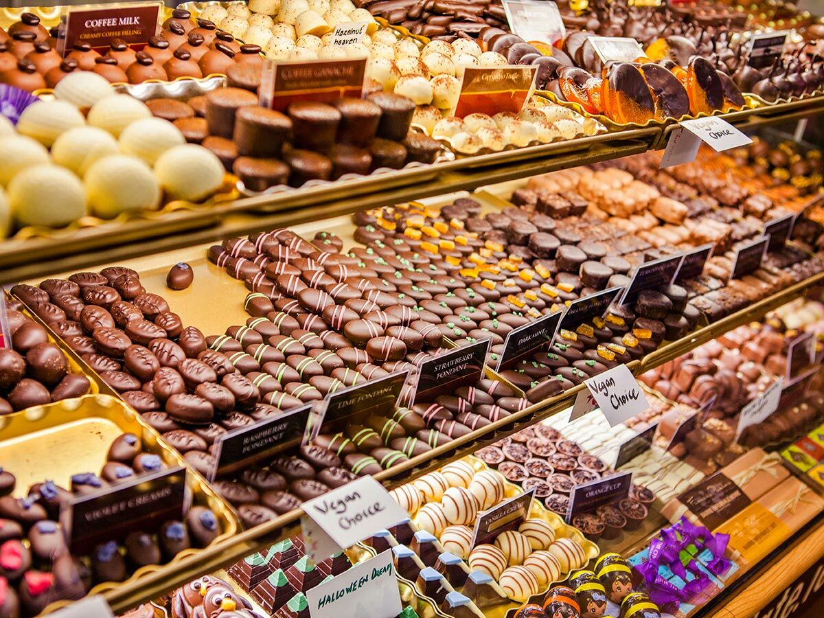 Reiche Auswahl an handgemachten Schokoladen und Pralinen in einer glänzenden Auslage, darunter vegane Optionen.