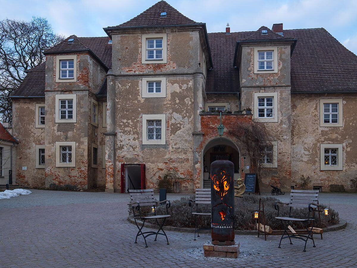 Altes Herrenhaus mit Innenhof, erleuchteter Feuersäule und gemütlichen Sitzgelegenheiten bei Dämmerung im Winter.