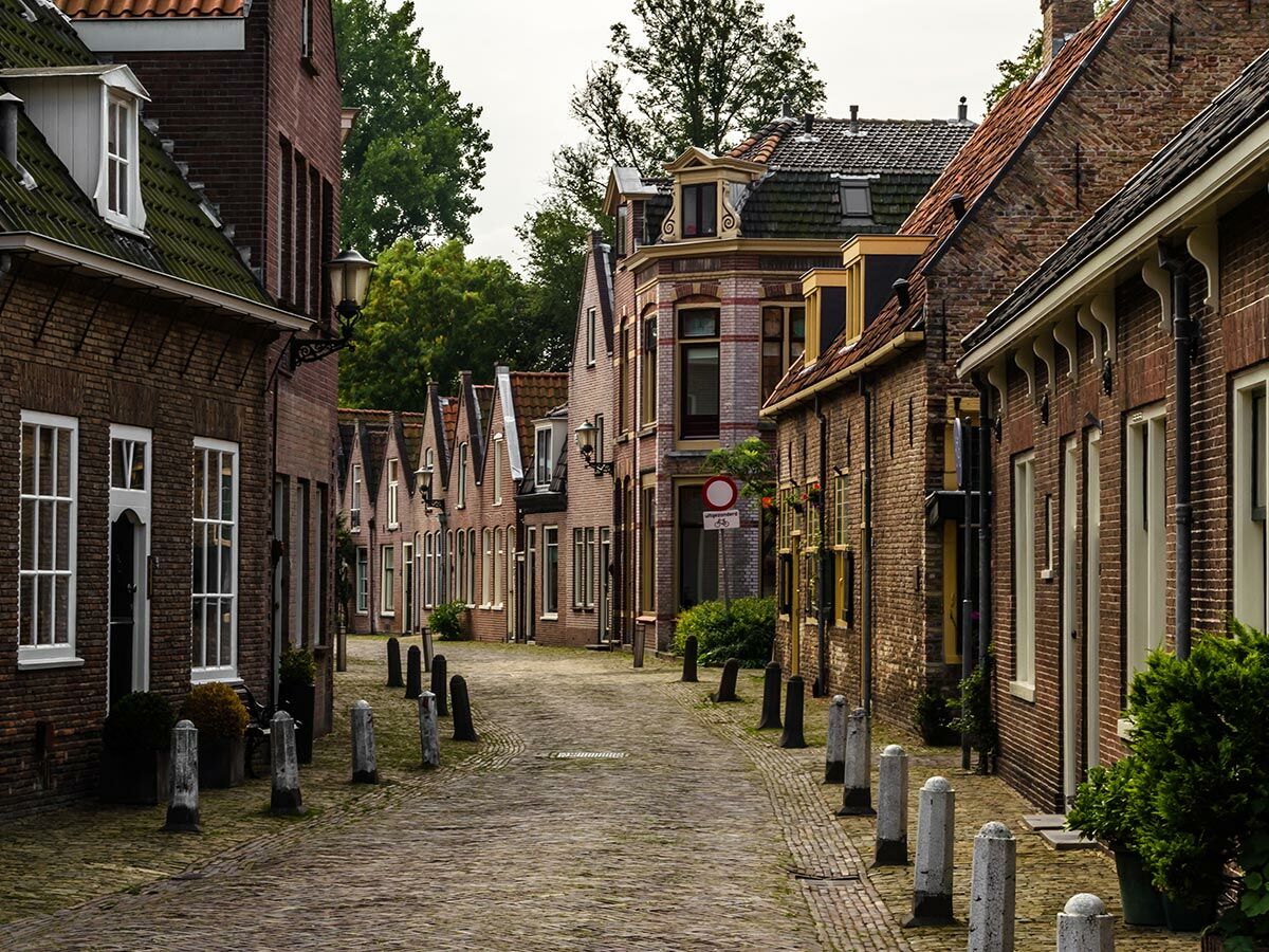 Blick auf eine charmante historische Gasse mit Backsteinhäusern, Kopfsteinpflaster und Pollern in einem alten Dorf.
