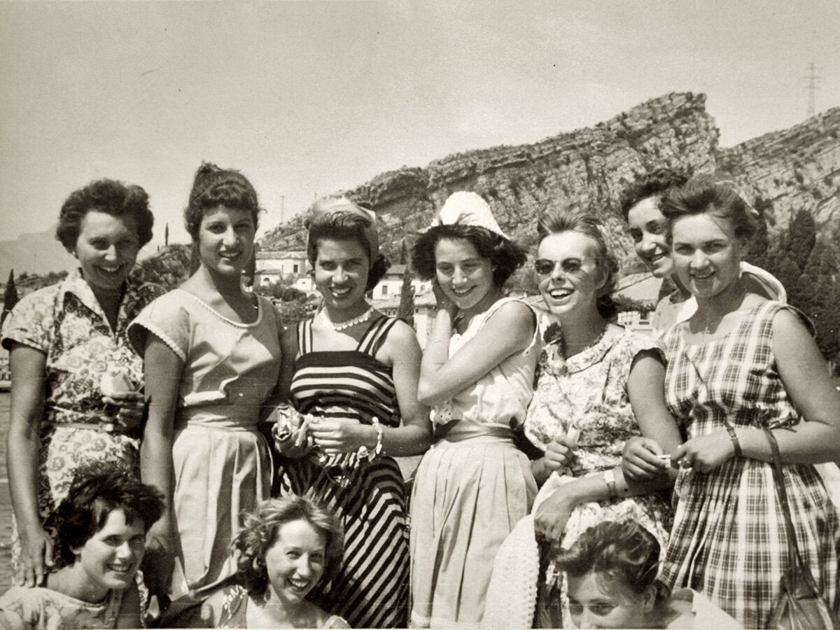 Schwarz-Weiß-Foto einer großen, lachenden Frauengruppe in Sommerkleidung vor Bergen und See, typisch 1950er/60er Jahre.