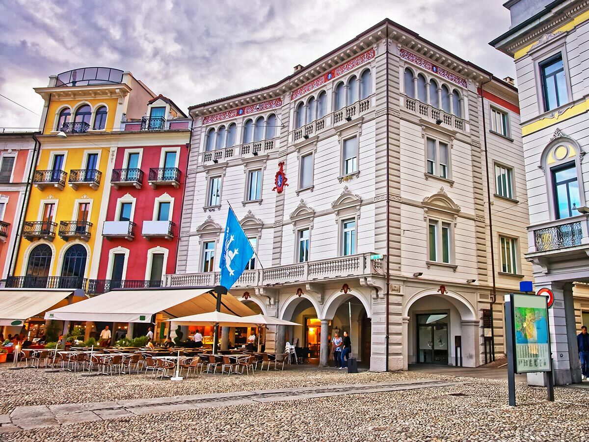 Belebter europäischer Stadtplatz mit farbenfrohen Gebäuden, Außengastronomie und Kopfsteinpflaster. Historische Architektur.