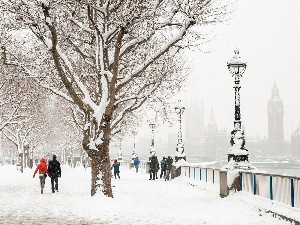 Zwei Personen gehen auf verschneitem Weg entlang der Themse, mit Blick auf Westminster und Big Ben.
