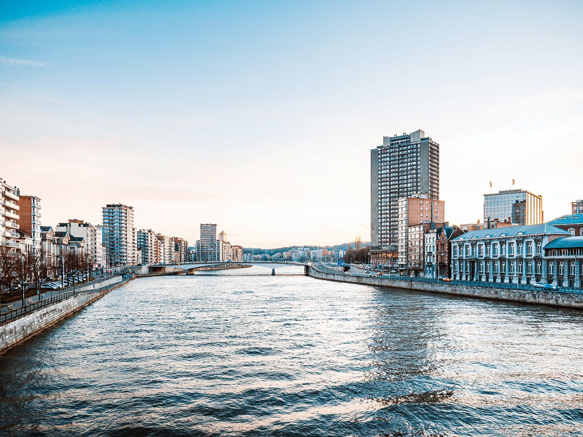 Panoramablick auf den Maasfluss in Liège mit Stadtgebäuden, Brücken und klarem Himmel am Abend.