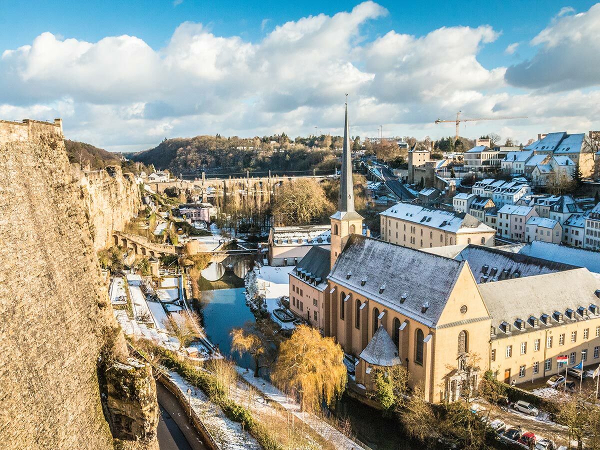 Panoramablick auf die verschneite Altstadt von Luxemburg mit Abtei Neumünster, Fluss Alzette und Festungsmauern im Winter.