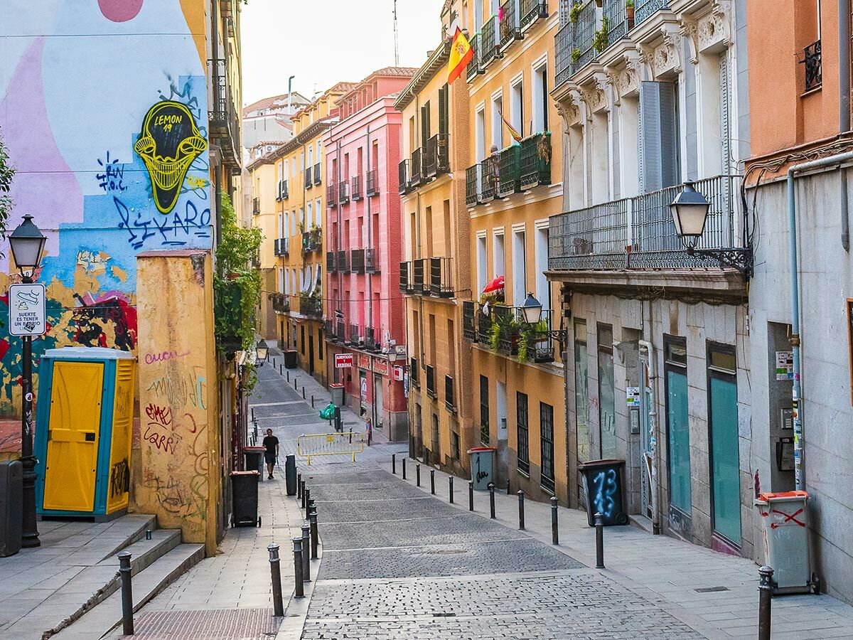Schmale, bunte Gasse in Madrid mit historischen Gebäuden, Graffiti-Wand, Kopfsteinpflaster und einer Person.