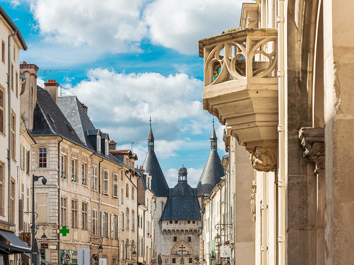 Blick durch eine Gasse in Tournus, Frankreich, auf die Porte de l'Horloge mit Türmen und einem kunstvollen Balkon.