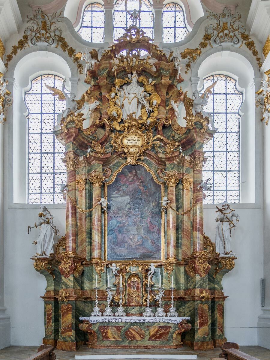 Detailreicher barocker Hochaltar mit Marmorsäulen, Goldornamenten, Statuen und einem Gemälde in einer Kirche.