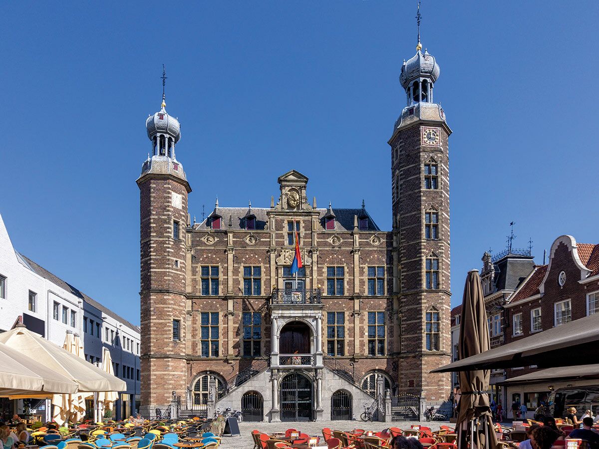 Historisches Rathaus Middelburg, Niederlande, mit zwei Türmen und belebtem Marktplatz mit Außencafés unter blauem Himmel.