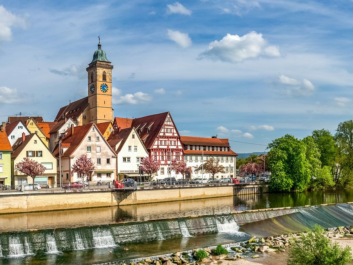 Lauffen am Neckar: Blick auf Regiswindiskirche, Fachwerkhäuser und den Neckar mit Wehr im Frühling.