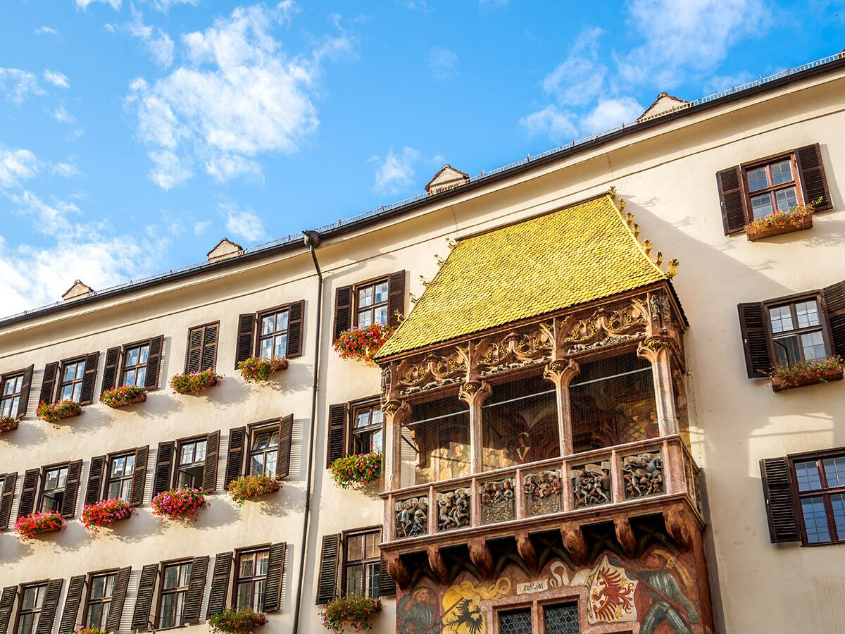 Das berühmte Goldene Dachl in Innsbruck, Österreich, mit seiner goldenen Balustrade, geschnitzten Verzierungen und Blumenkästen unter blauem Himmel.