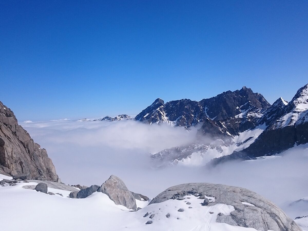 Majestätisches Alpenpanorama mit schnee- und felsbedeckten Gipfeln, die aus einem dichten Wolkenmeer unter blauem Himmel ragen.