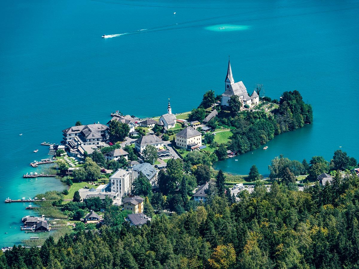 Luftaufnahme der malerischen Inselkirche auf einer bewaldeten Insel im türkisfarbenen Bleder See, umgeben von Häusern und Wäldern.