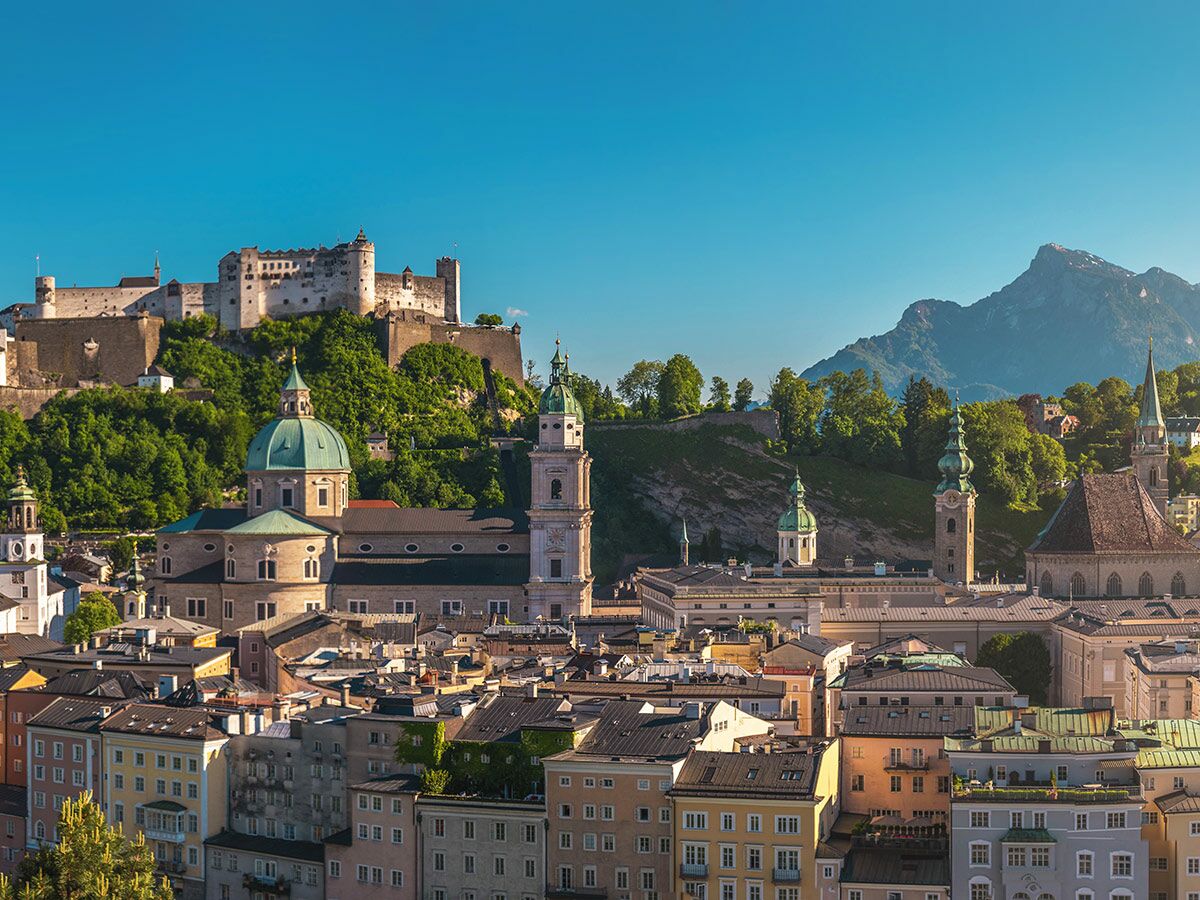 Panoramablick auf Salzburg mit Hohensalzburg Festung, Dom und Alpen im Hintergrund bei strahlendem Sonnenschein.