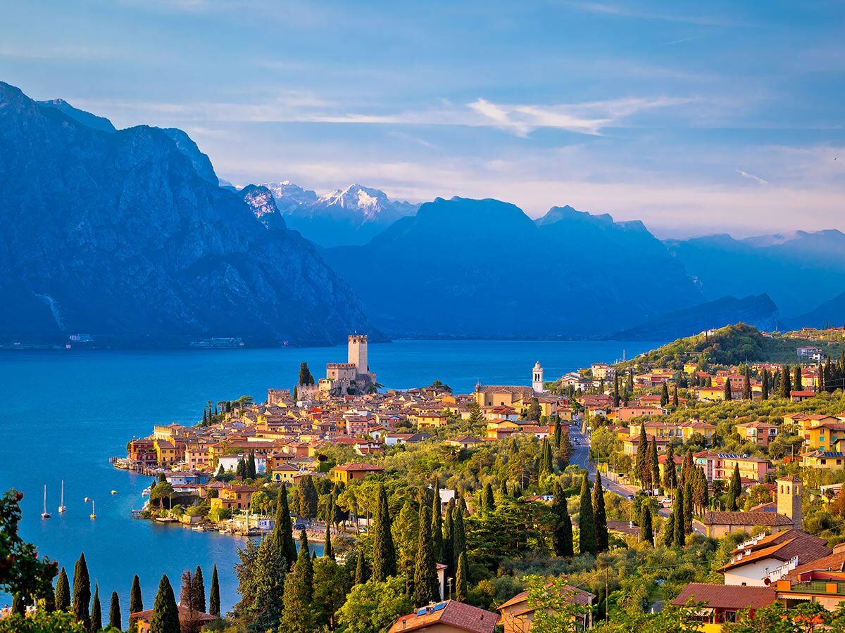 Panorama von Malcesine am Gardasee mit Scaliger-Schloss, bunten Häusern und Alpen im Hintergrund unter blauem Himmel.