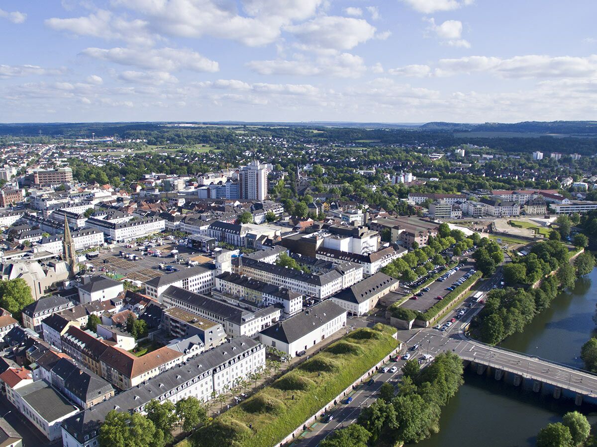 Luftaufnahme von Saarlouis mit Saar-Fluss, Brücke, Stadtzentrum, historischen Gebäuden, Wallanlagen und grünem Umland unter Wolken.