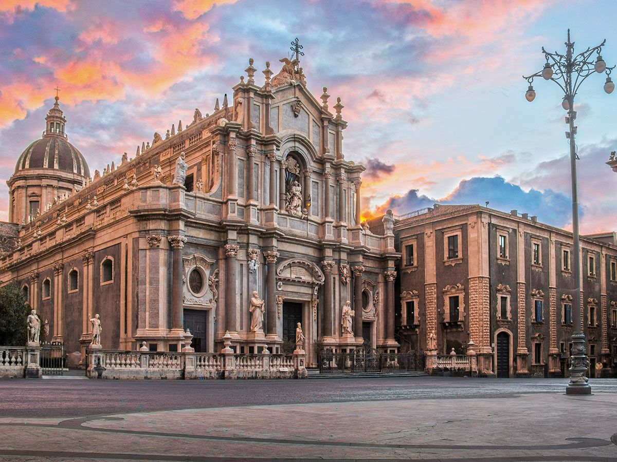Majestätische Kathedrale von Catania bei Sonnenuntergang mit farbenprächtigem Himmel und historischen Gebäuden auf der Piazza Duomo, Sizilien.